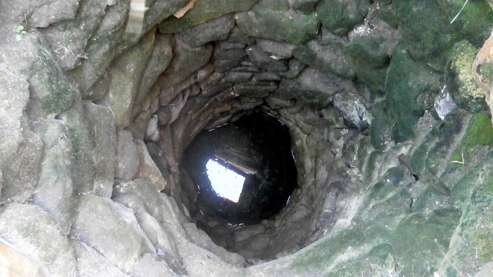 Puits traditionnel en pierre vu du dessus, eau au fond